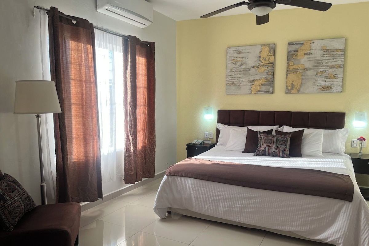 Una habitación de hotel con una cama grande, un escritorio, una silla y dos lámparas fijadas a la pared.
