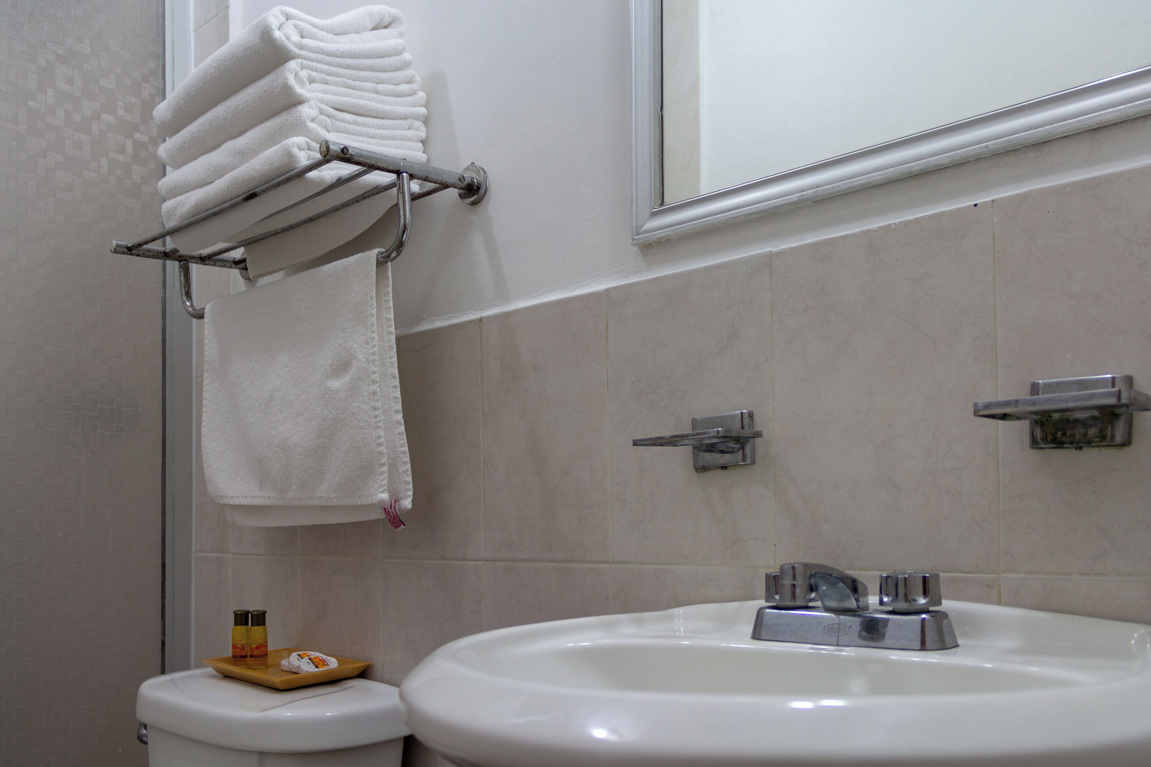 Un baño con un lavamanos blanco, un perchero con toallas dobladas, un inodoro y un espejo sobre el lavamanos.