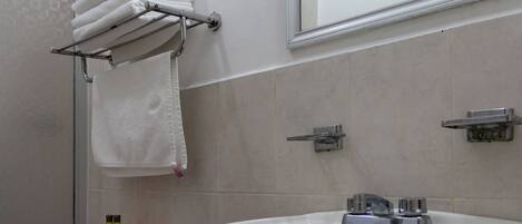 Un baño con un lavamanos blanco, un perchero con toallas dobladas, un inodoro y un espejo sobre el lavamanos.
