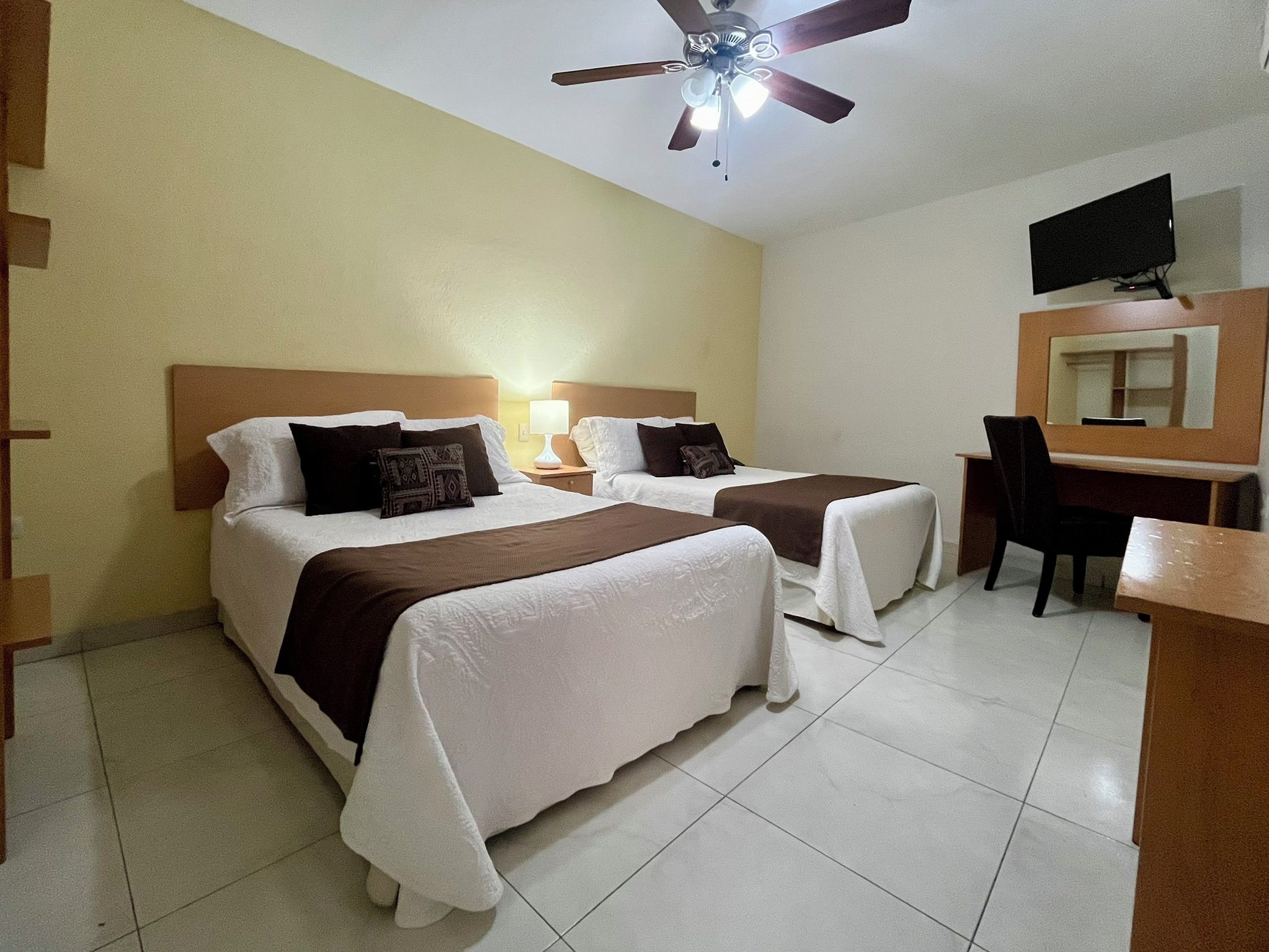 Habitación de hotel con dos camas, un escritorio, una silla, un televisor y un ventilador de techo.