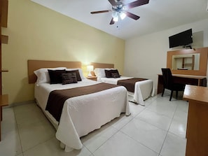 Habitación de hotel con dos camas, un escritorio, una silla, un televisor y un ventilador de techo.