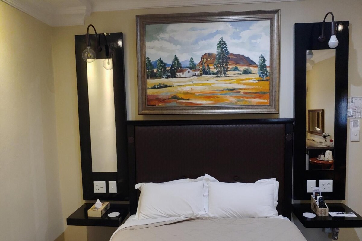 Une chambre d’hôtel avec un lit, un tableau au-dessus de la tête de lit, une table de chevet avec une lampe et un miroir.