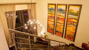 A staircase with a metal railing, a chandelier, and three landscape paintings on the wall.