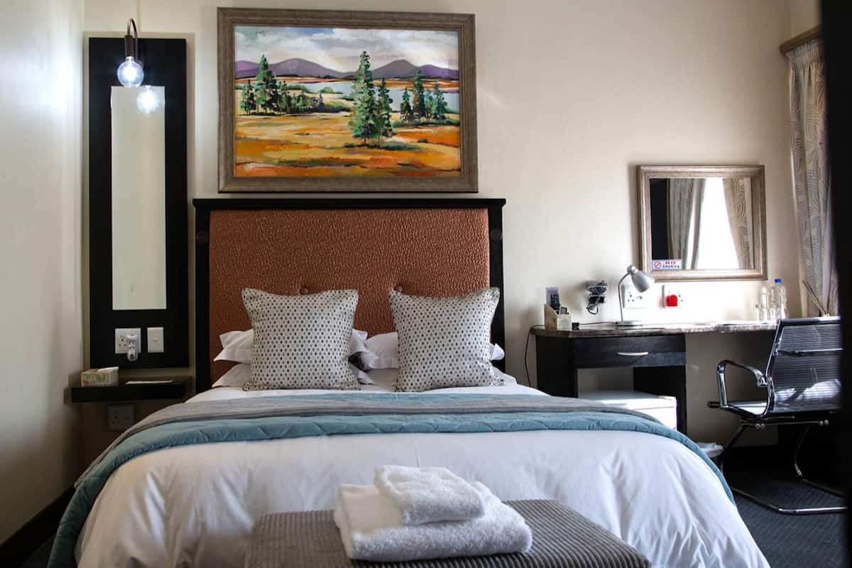 Une chambre d’hôtel avec un lit, un bureau, une chaise, un tableau et une lampe.