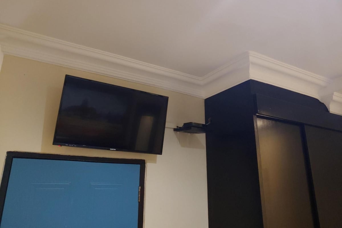 Een kamer met een wandgemonteerde flatscreen-tv, een blauwe deur en een zwarte kast.