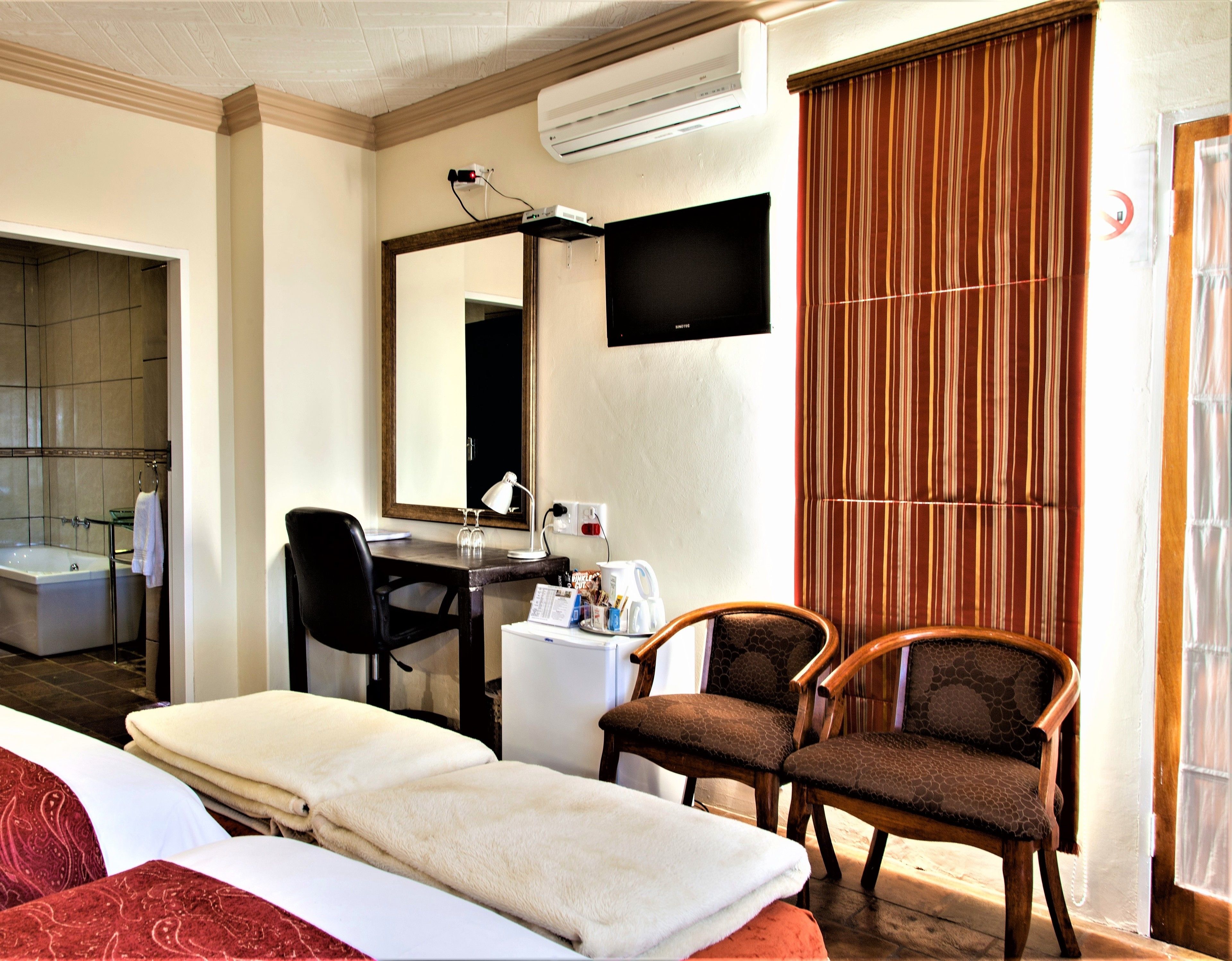 A hotel room with a bed, a desk with a chair, a TV, and a window with curtains.