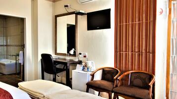 A hotel room with a bed, a desk with a chair, a TV, and a window with curtains.