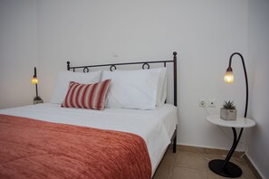 Una cama bien hecha con una colcha roja, almohadas blancas y una almohada a rayas rojas y blancas. Hay dos lámparas de noche a ambos lados de la cama.