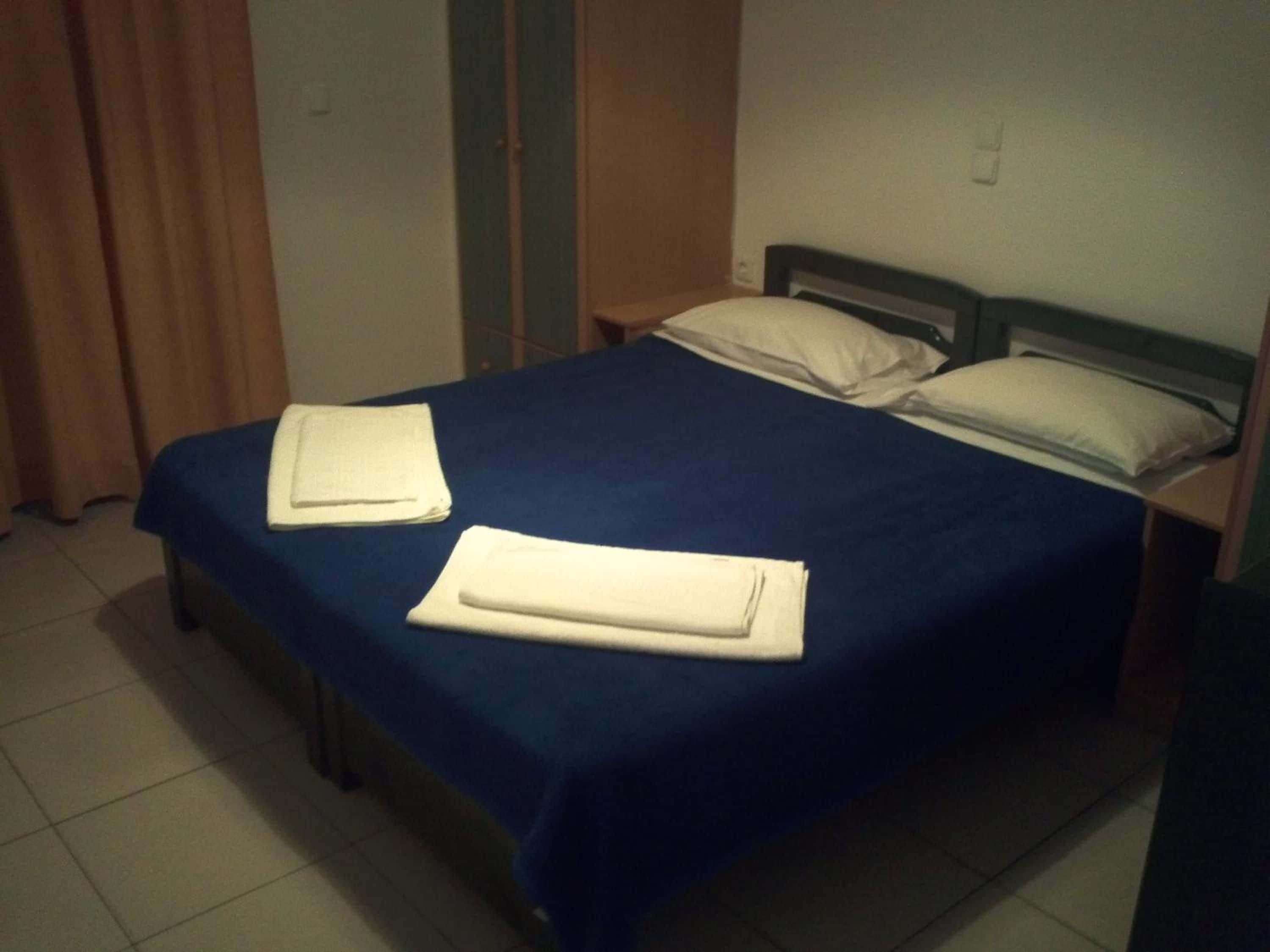 Ein Einzelbett mit blauer Bettdecke und zwei Kissen, ein gefaltetes weißes Handtuch auf dem Bett sowie ein hölzernes Kopfteil.