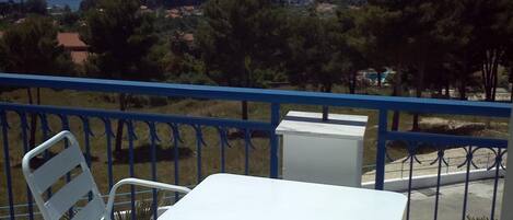 A balcony with a white table and chairs, overlooking a coastal landscape.