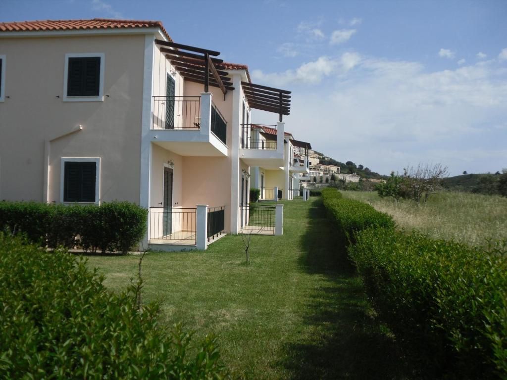 A row of modern two-story residential buildings with balconies, a well-maintained lawn, and a clear sky.