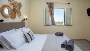 A hotel room with a bed, pillows, a view through a window, and wall decor. - Liberatos Village (Kefalonia)