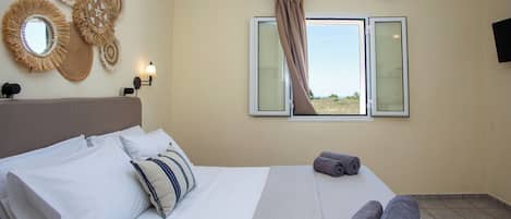 A hotel room with a bed, pillows, a view through a window, and wall decor.