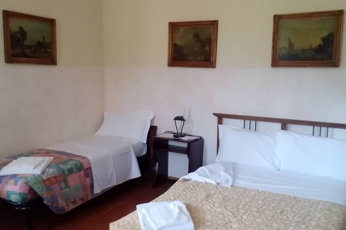 A hotel room with two beds, a nightstand, and three paintings on the wall.