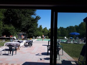 Une terrasse extérieure avec des tables et des chaises, une piscine et une pelouse.