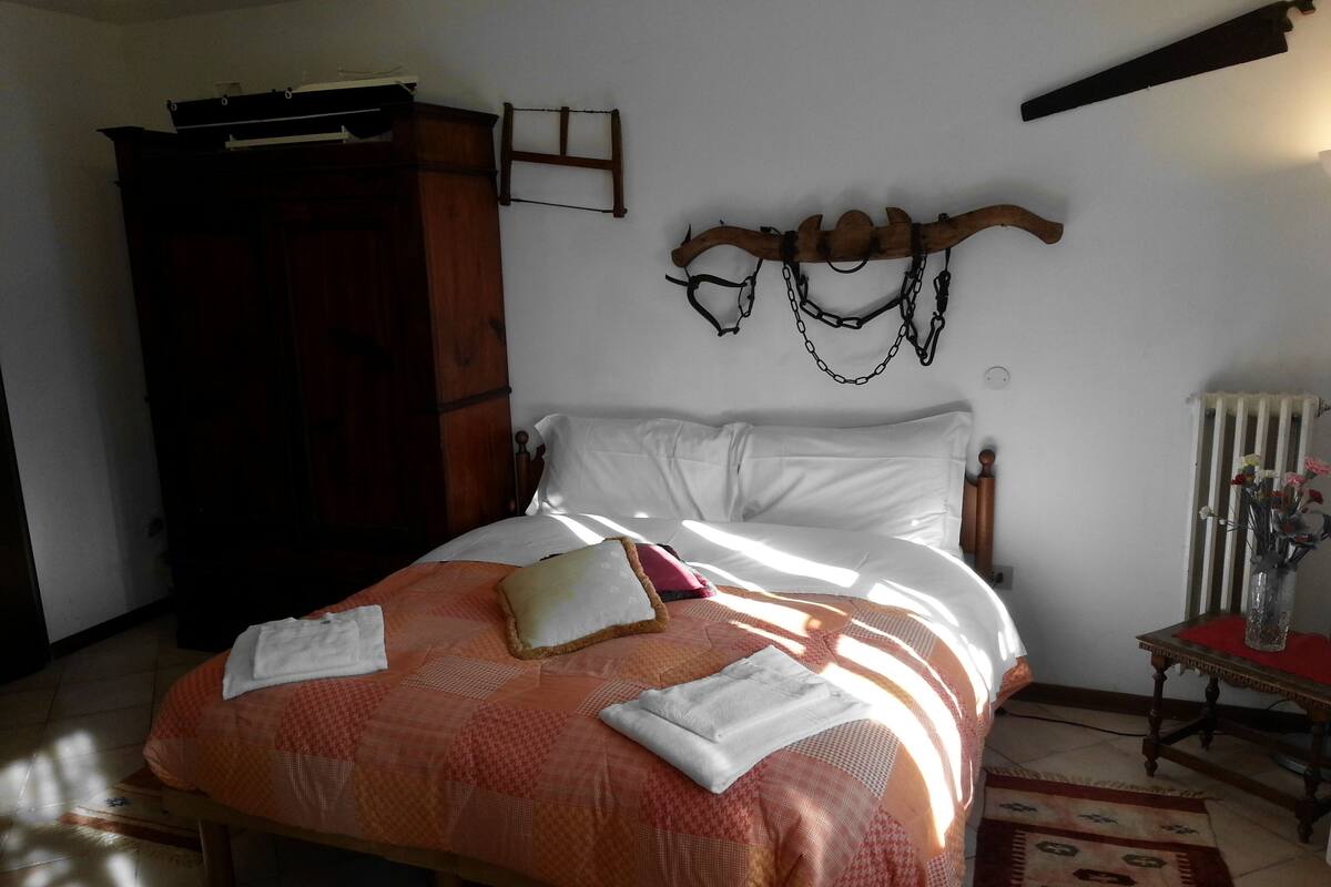 A bedroom with a bed, a wardrobe, a radiator, and a small table with a vase.