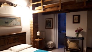 A bedroom with a bed, a nightstand, a chair, a table with a vase of flowers, and a painting on the wall. - Ecogarden (Mestre)