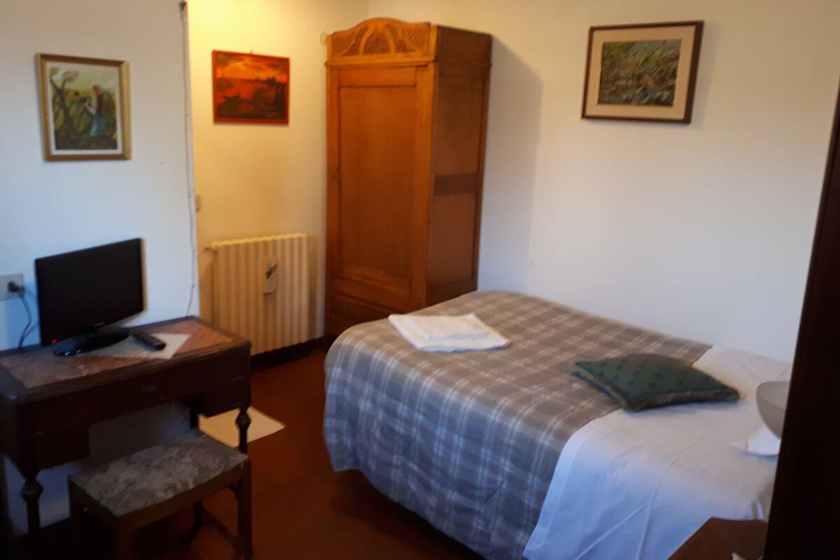 A bedroom with a bed, a desk, a chair, a wardrobe, and two framed pictures on the wall.