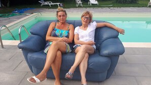Two people sitting on a blue outdoor sofa by a swimming pool. - Ecogarden (Mestre)