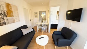 A modern living room with a black sofa, a blue armchair, a white coffee table, and a TV mounted on the wall. - Plesners Anneks (Skagen)