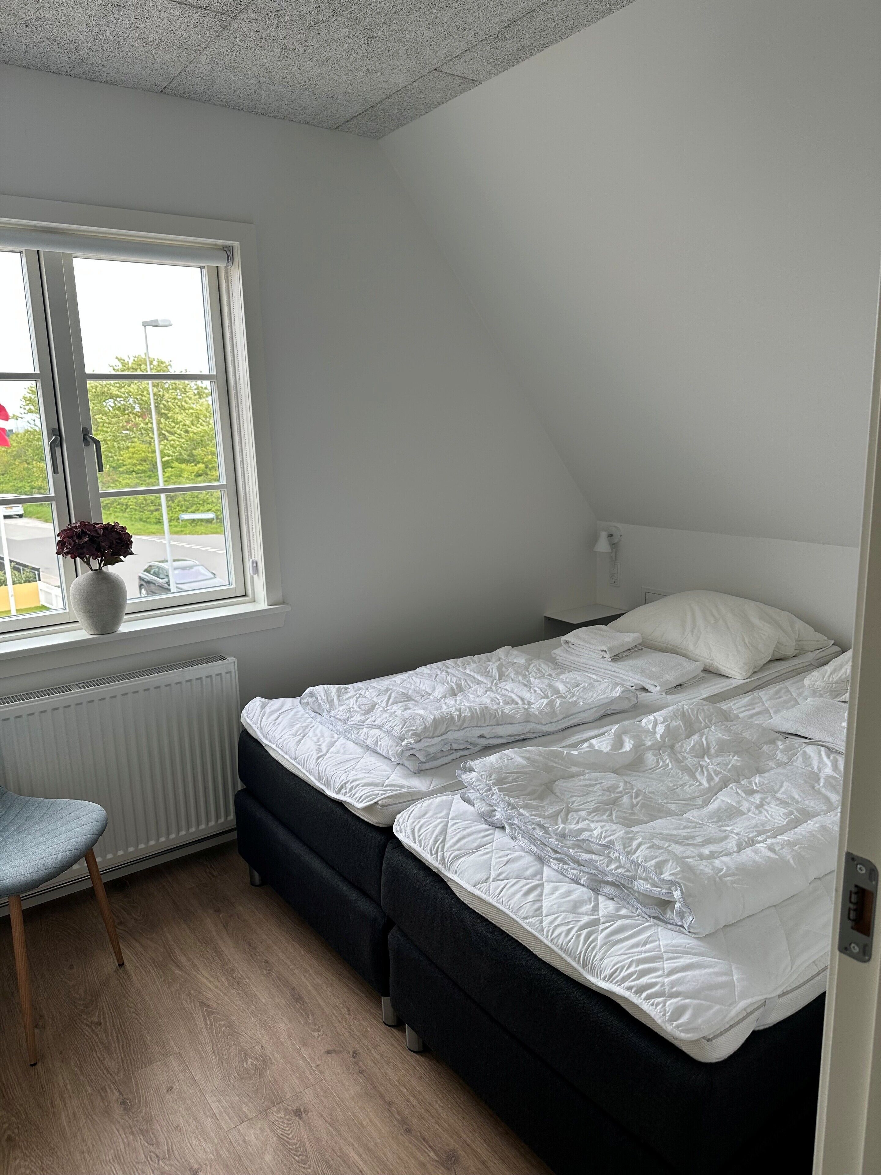 Een slaapkamer met een bed, een radiator, een raam en een stoel.