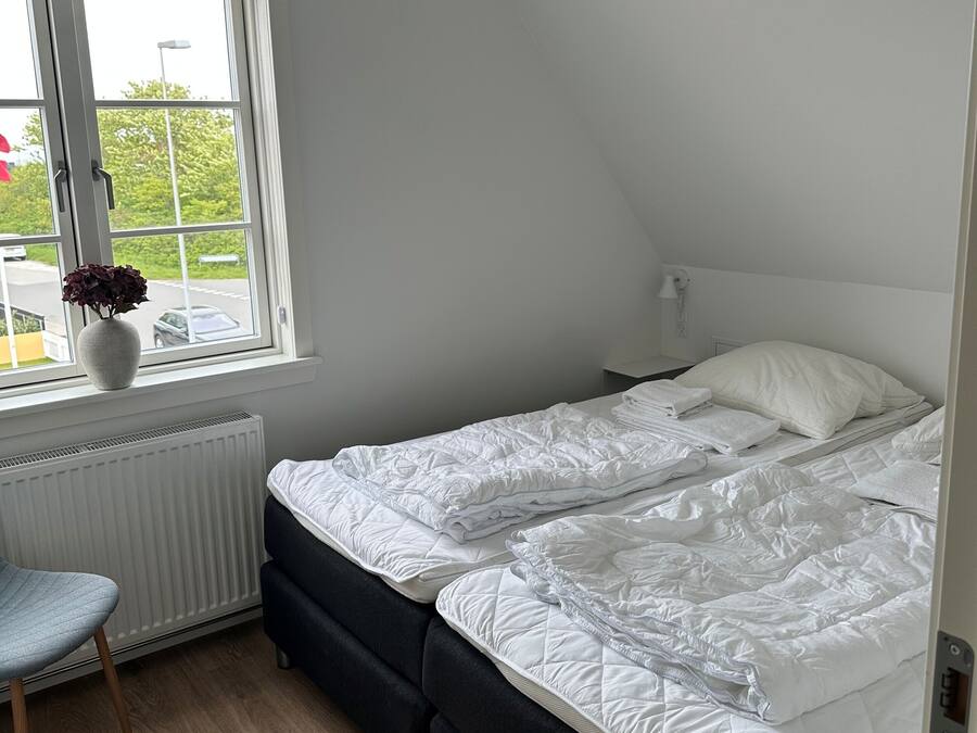 A bedroom with a bed, a radiator, a window, and a chair.
