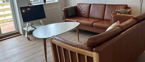 A modern living room with a brown leather sofa, a white coffee table, and a TV on a stand.