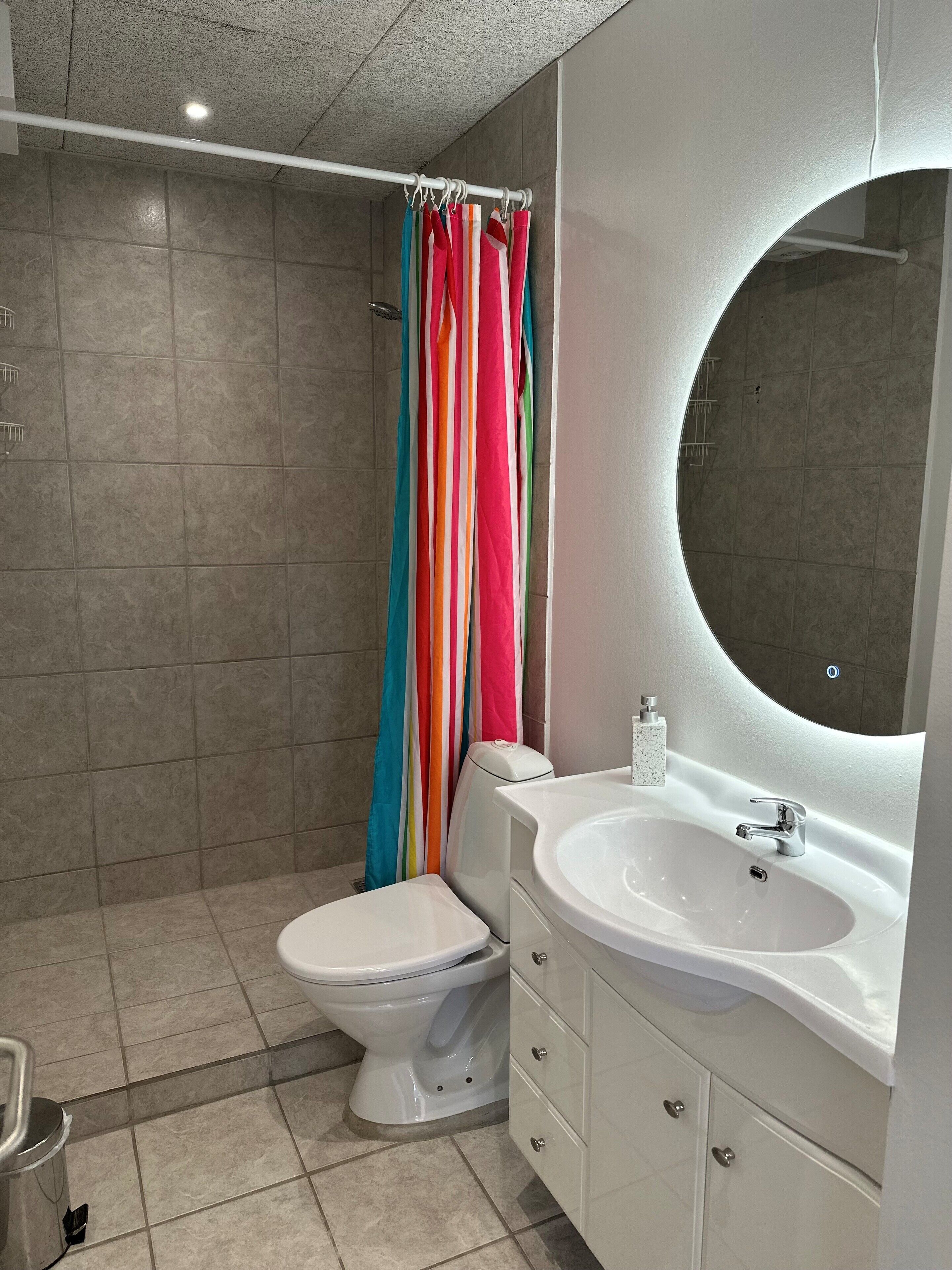 A bathroom with a white toilet, a white sink with a mirror, and a shower with a colorful striped curtain.