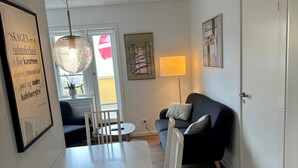 A modern living room with a dining area, featuring a white table and chairs, a black sofa, and a hanging light fixture. - Plesners Anneks (Skagen)