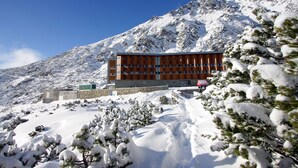 A hotel with a modern design, situated on a snowy mountain with a clear blue sky.