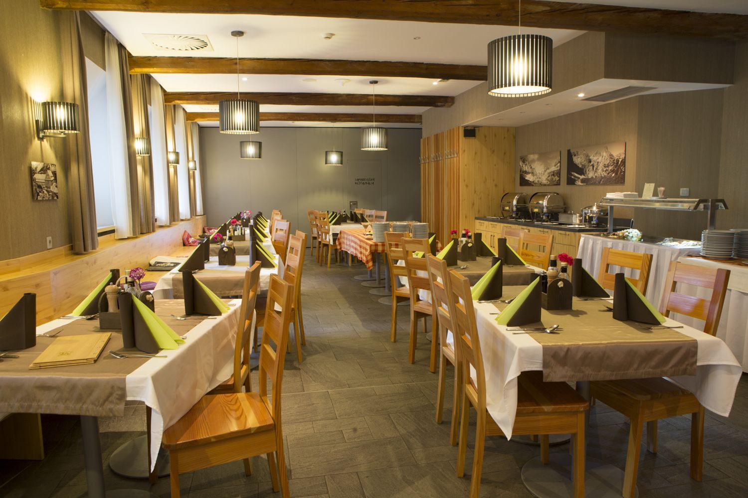 A restaurant with multiple tables, wooden chairs, and hanging pendant lights.