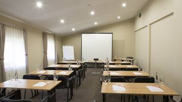 A conference room with multiple tables, chairs, a projector screen, and a whiteboard.