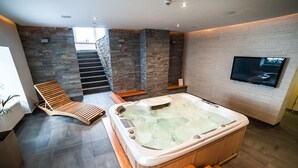 A modern spa area with a hot tub, wooden loungers, a staircase, and a mounted TV.