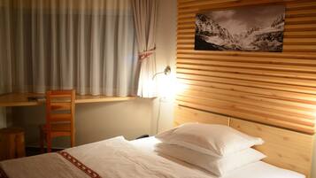 Un dormitorio con cabecera de madera, cama con ropa blanca, escritorio con silla y ventana con cortinas.