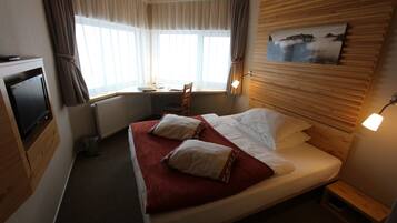 Habitación de hotel con cama, escritorio, silla, televisor y ventana con cortinas.