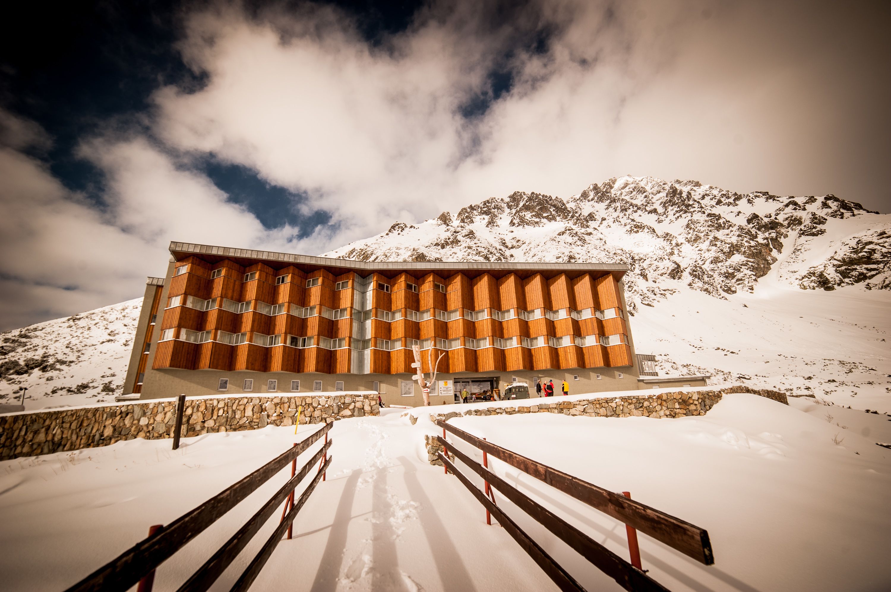 A modern building with a unique wooden facade, surrounded by snow-covered mountains.