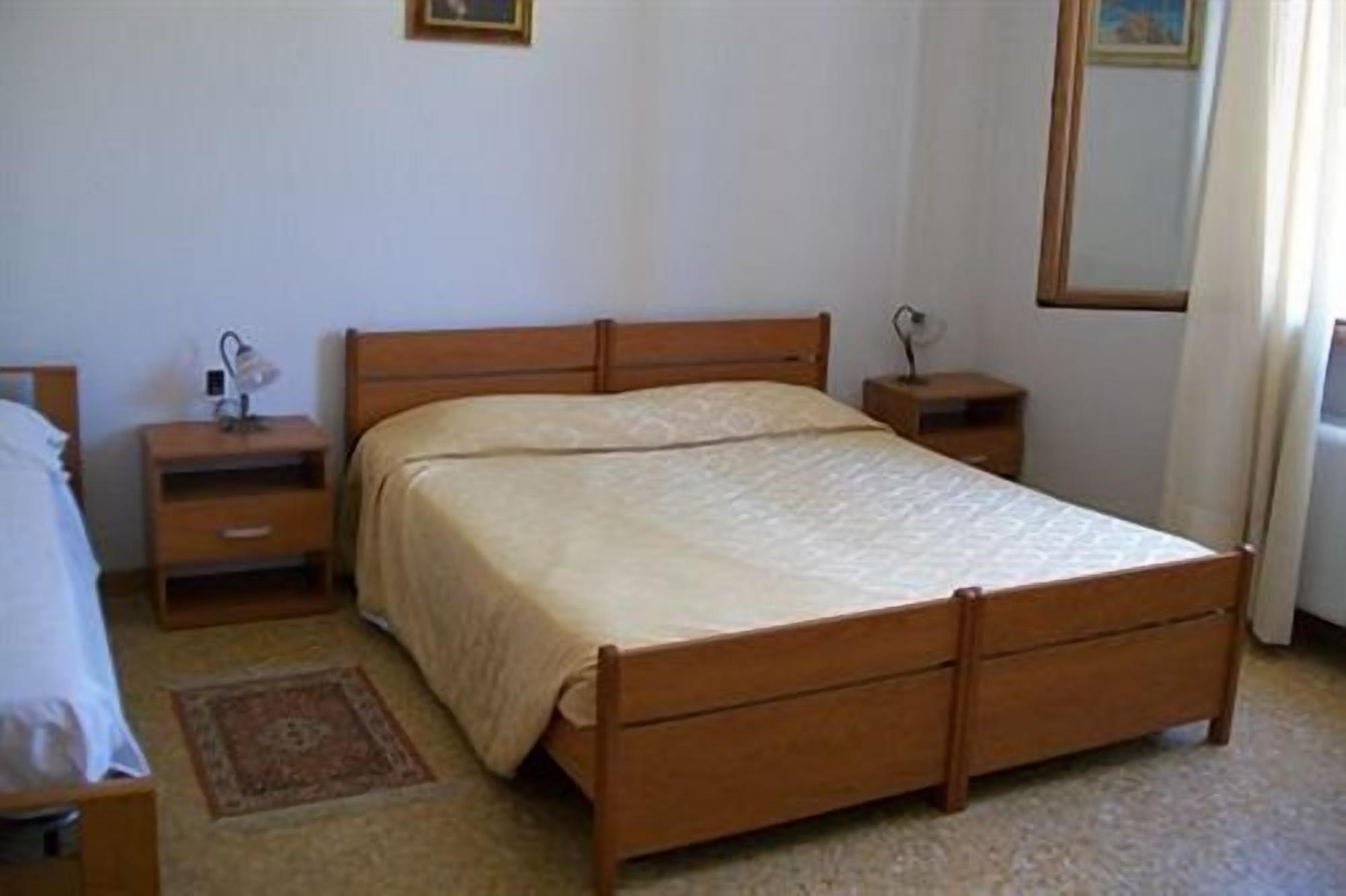Een slaapkamer met een houten bed, nachtkastje, bijzettafeltje en een klein vloerkleed.
