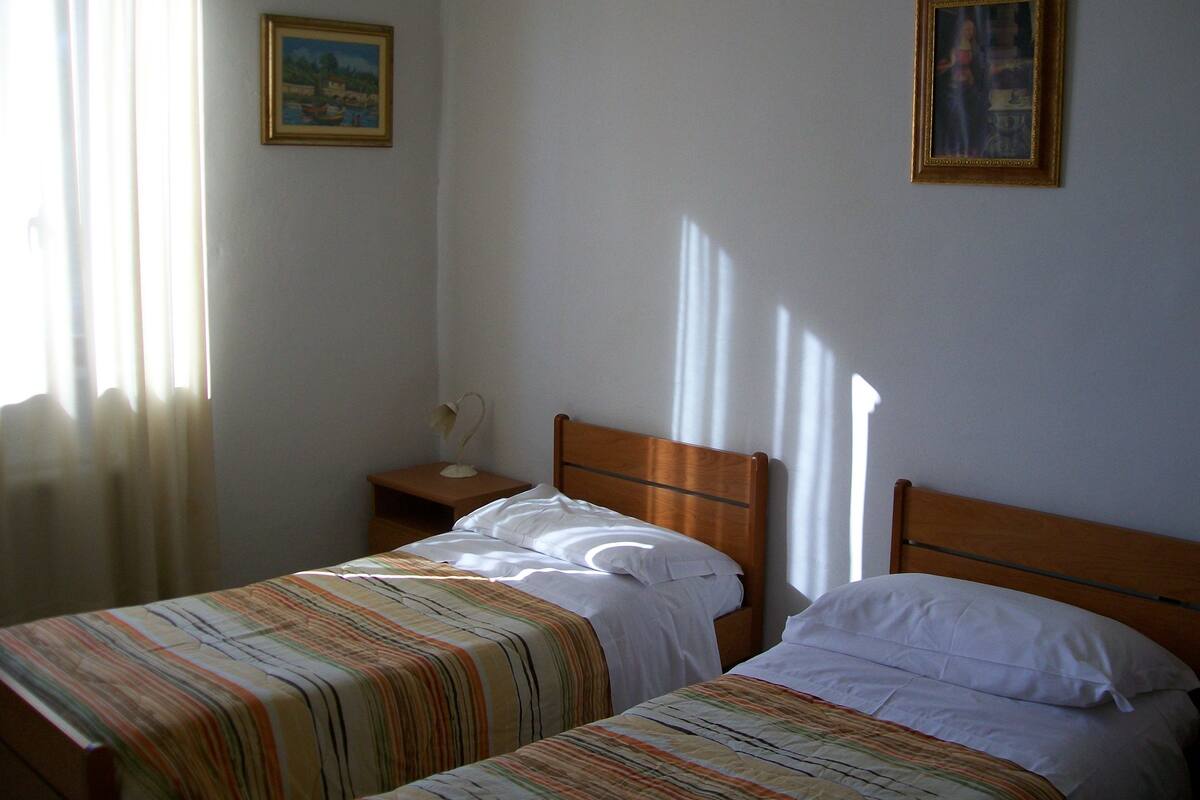 A room with two beds, a nightstand, and two framed pictures on the wall.