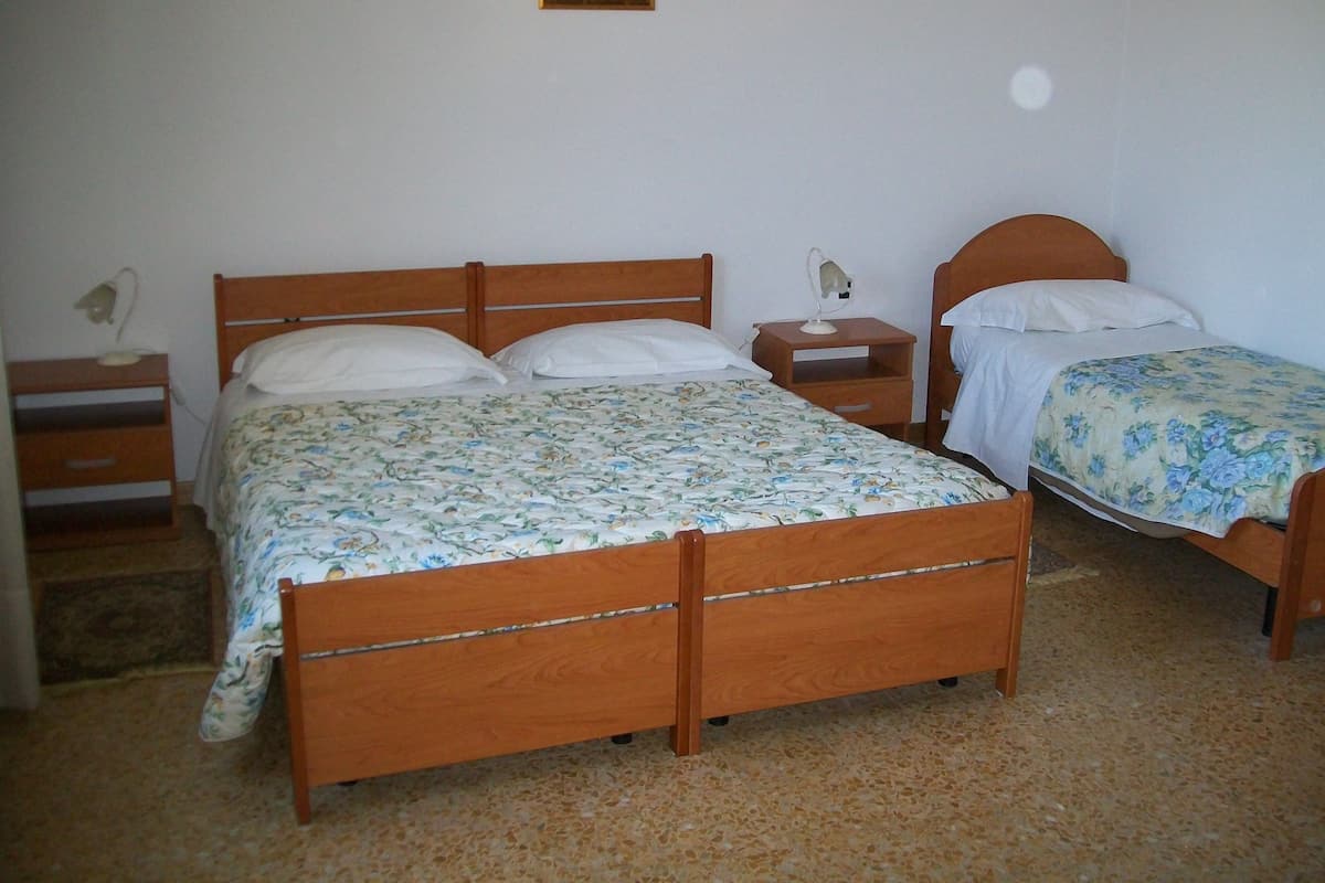 A bedroom with two wooden beds, a nightstand, a bedside table, and a wall-mounted lamp.
