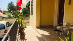 A building with a yellow exterior, a tiled patio, a potted plant, a table with chairs, and flags. - Bed & Breakfast Locanda La Rotonda (Montale)
