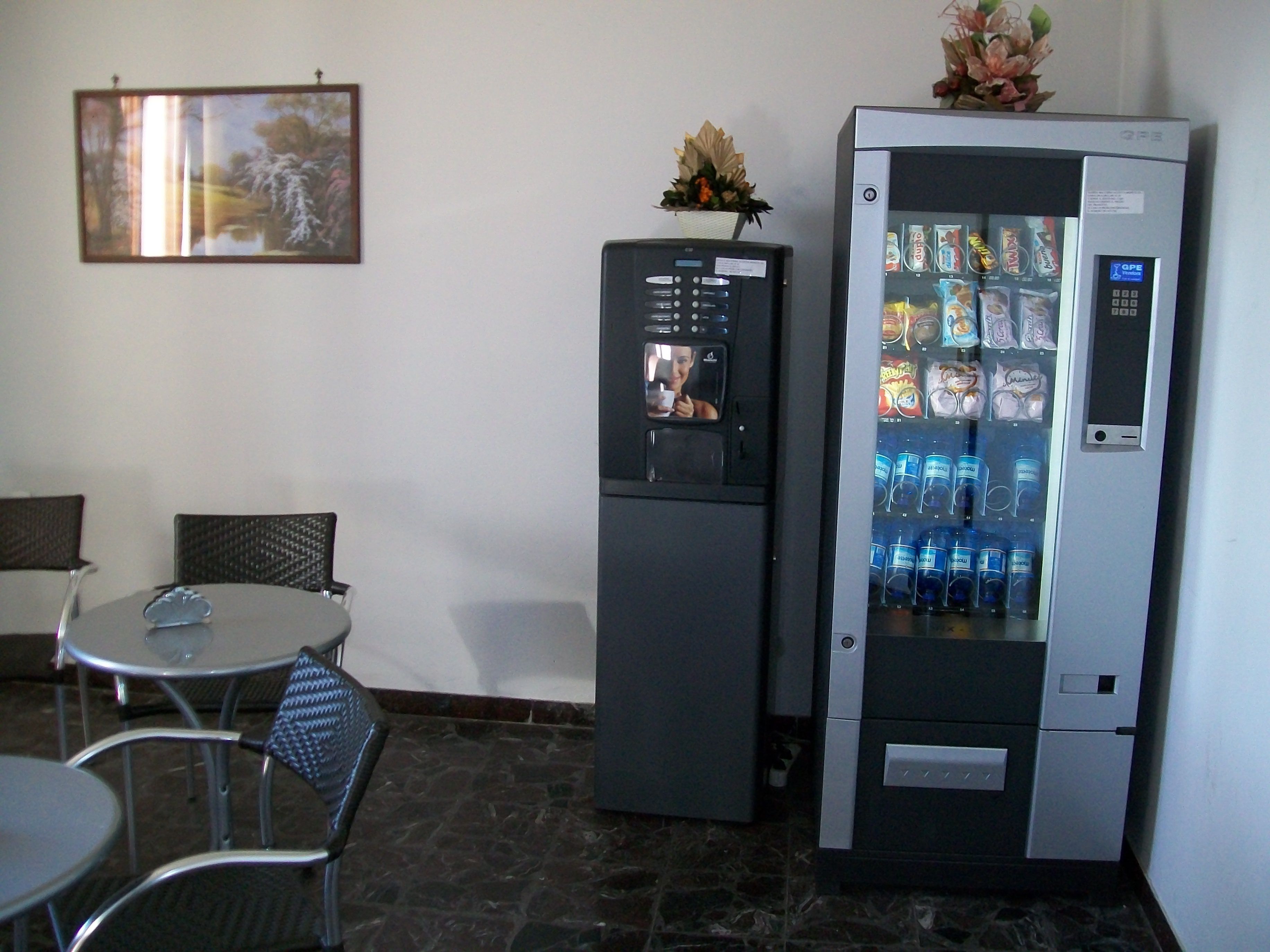 Una habitación con una pequeña mesa y sillas, un refrigerador y una máquina expendedora.