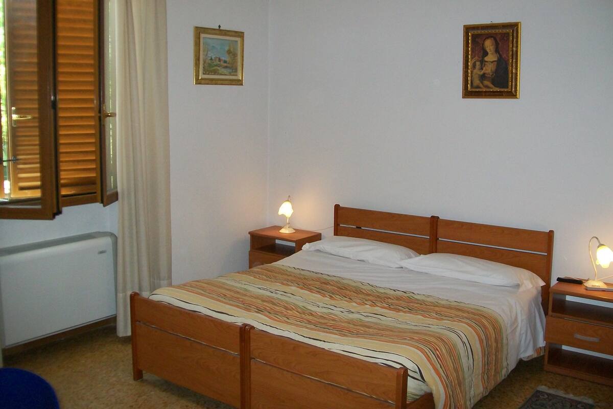 A bedroom with a wooden bed, two bedside lamps, a radiator, and two framed pictures on the wall.