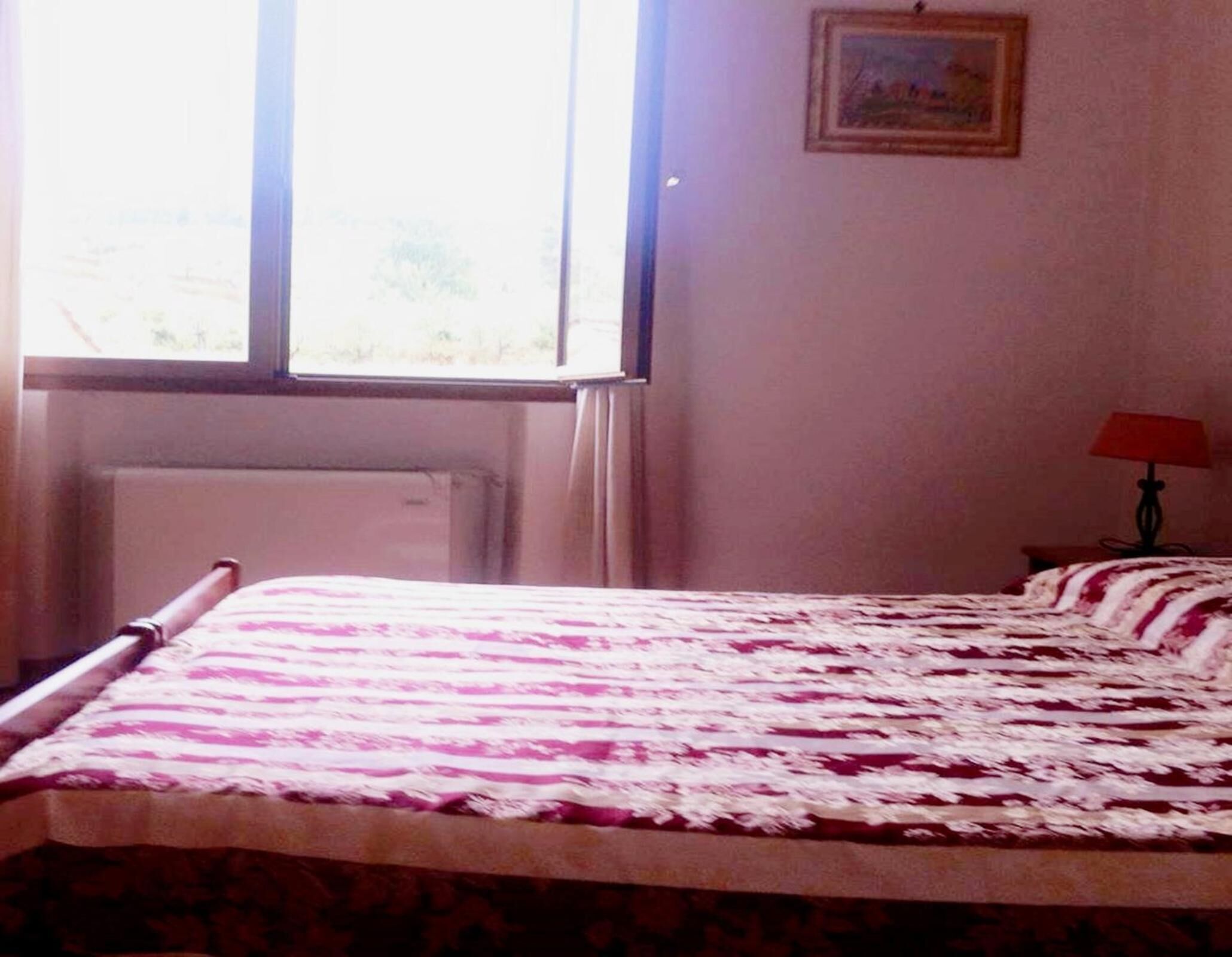 Un dormitorio con cama, ventana, radiador y lámpara.