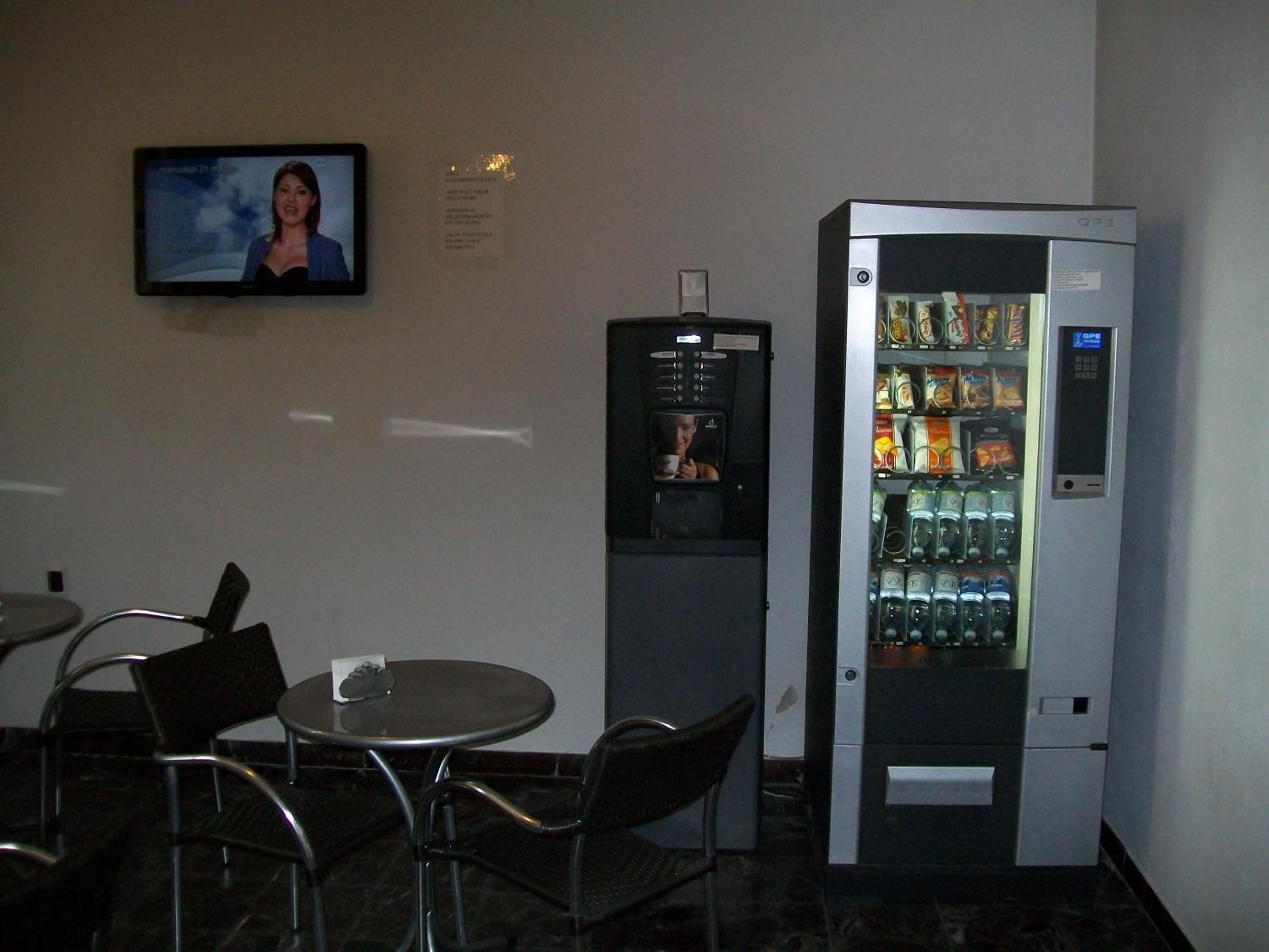 Un pequeño espacio interior con una disposición de asientos, una máquina expendedora de bebidas y un televisor montado en la pared.