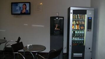 Un pequeño espacio interior con una disposición de asientos, una máquina expendedora de bebidas y un televisor montado en la pared.