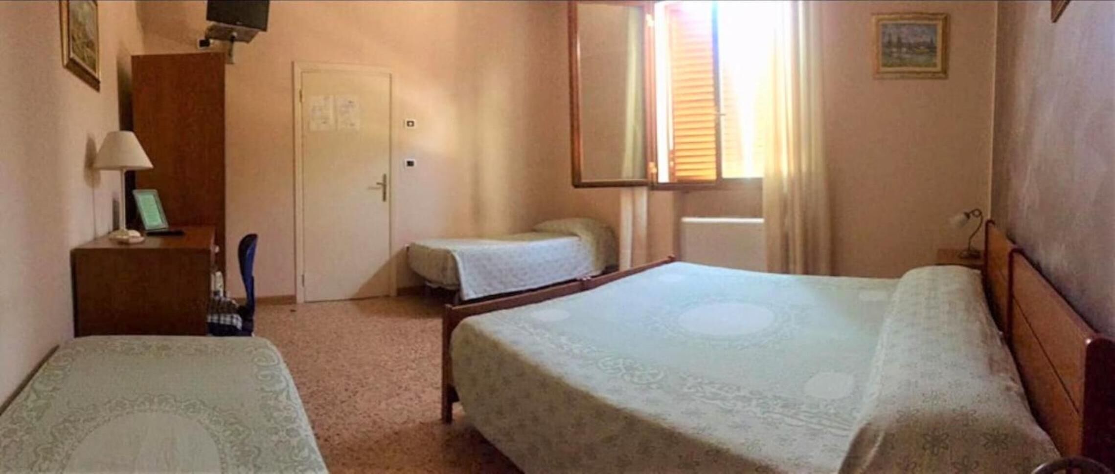 Et hotelværelse med to senge, et skrivebord med lampe, et klædeskab og et vindue med persienner.