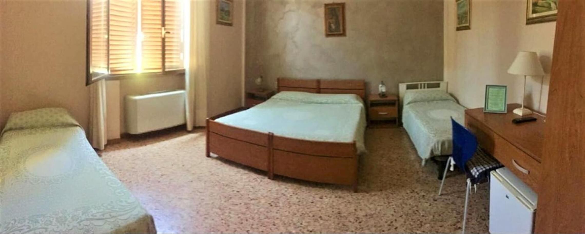 Un dormitorio con una cama grande, dos camas más pequeñas, un aparador, una mesita de noche y un radiador.