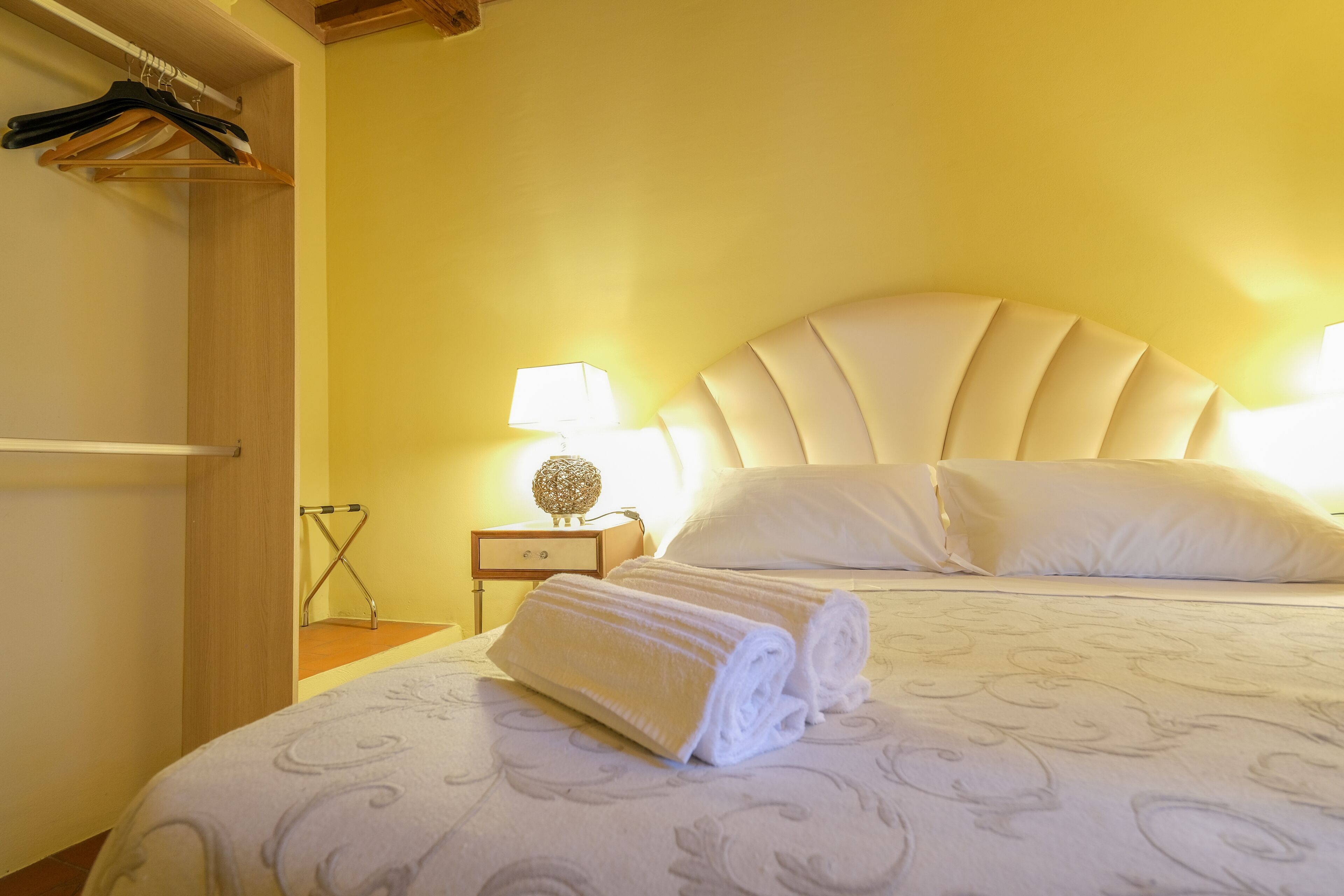 Une chambre d’hôtel avec un lit, une table de chevet, une lampe et une serviette posée sur le lit.