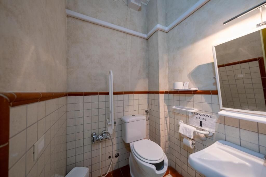 A small, compact bathroom with a toilet, sink, and shower. A sign indicates the flush direction.