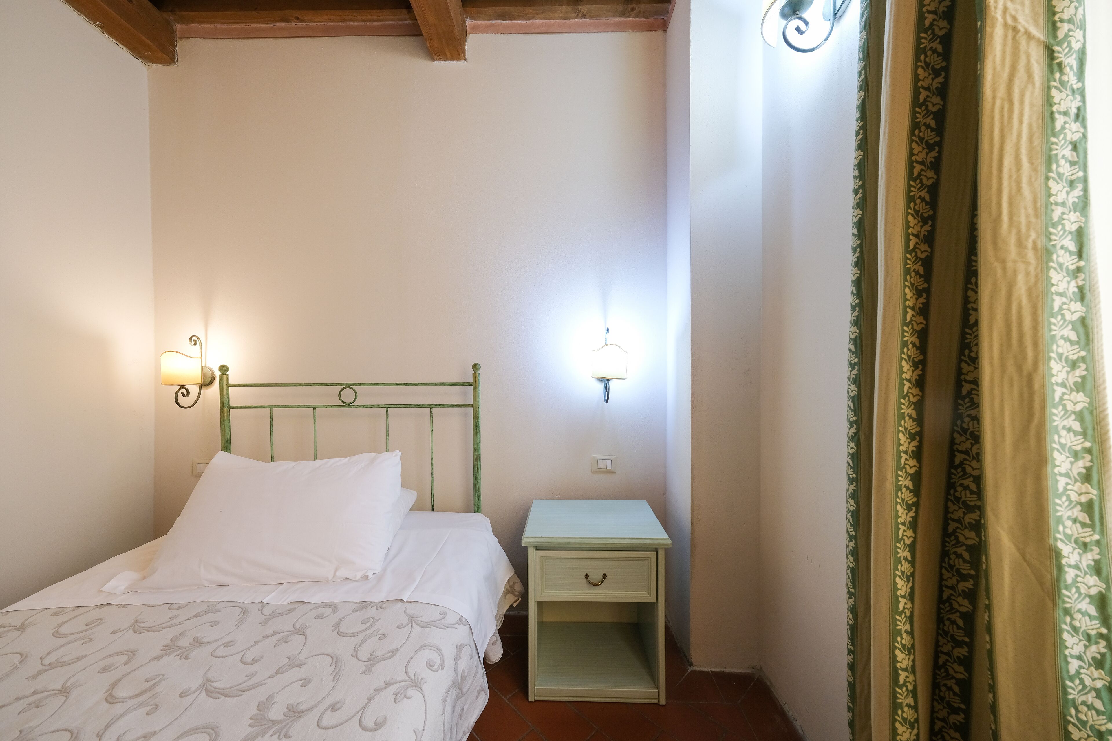 A bedroom with a bed, a nightstand, a wall-mounted light, and a curtain.